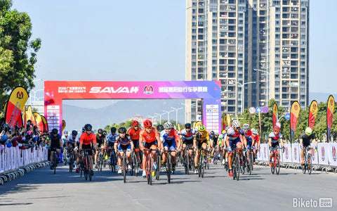 Cyclists racing on SAVA carbon bikes at a city event with SAVA banner and crowd cheering.