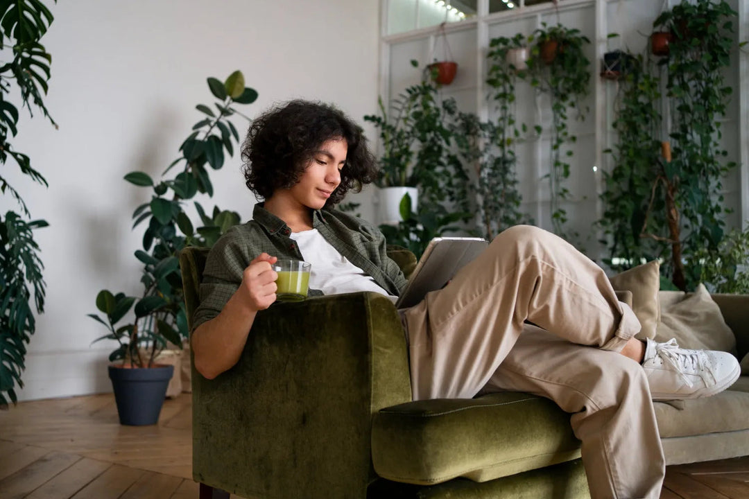 Person relaxing on green armchair reading tablet, surrounded by indoor plants