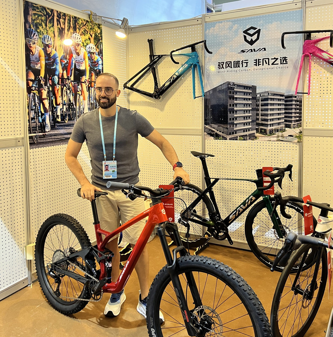 Man standing with SAVA carbon bike at trade show booth displaying mountain and road bikes