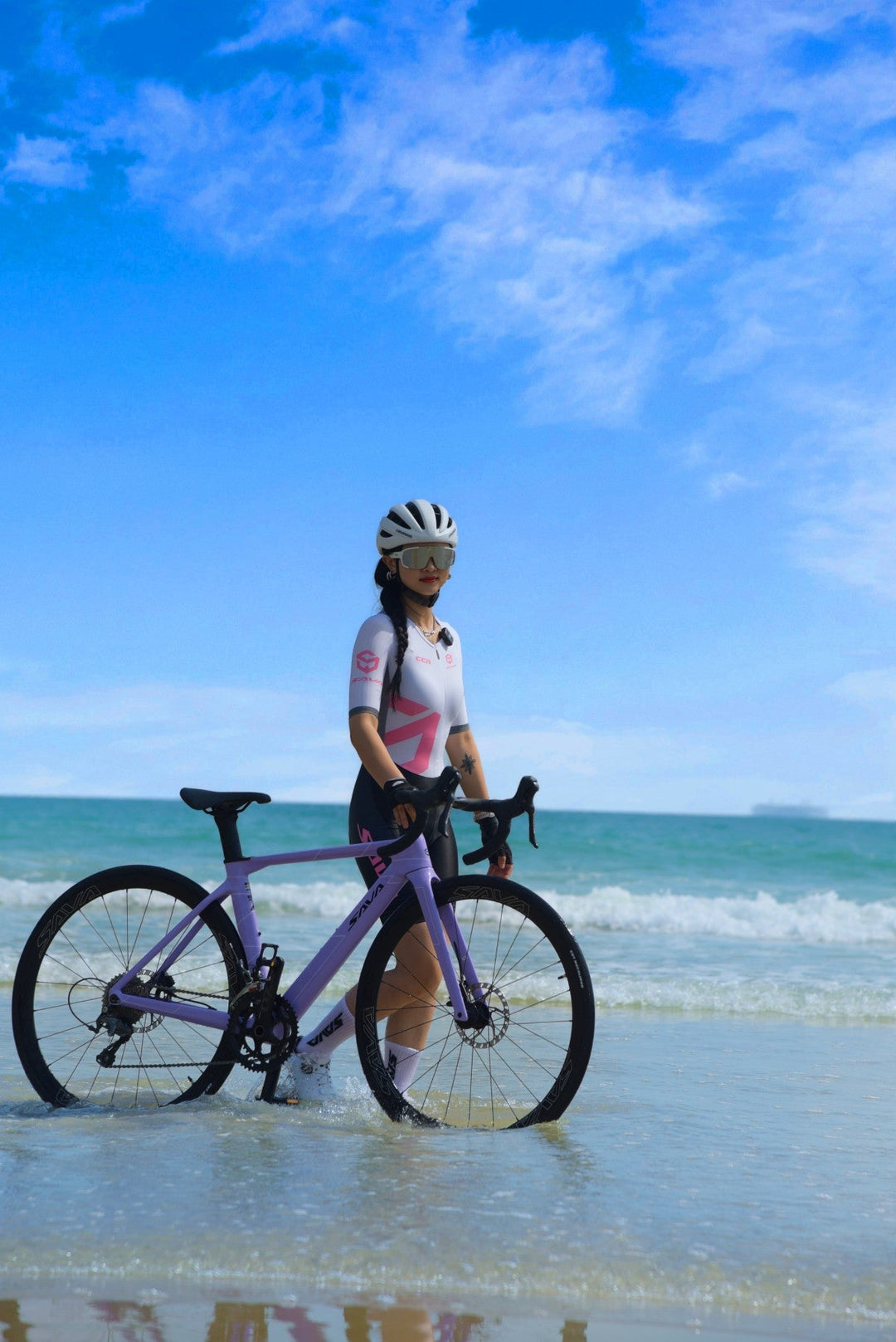 Cyclist with SAVA carbon road bike standing on beach shore under blue sky