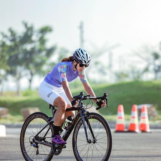 Cyclist riding SAVA carbon road bike outdoors, wearing helmet, passing traffic cones on pavement