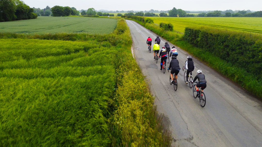 Cyclists ride SAVA carbon bikes on a rural road surrounded by green fields and hedges