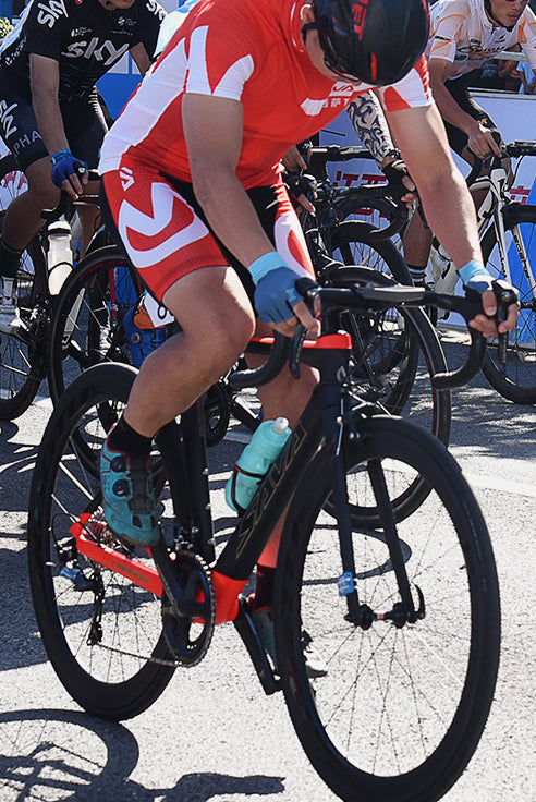Cyclist riding SAVA carbon road bike in a race, wearing red kit and helmet