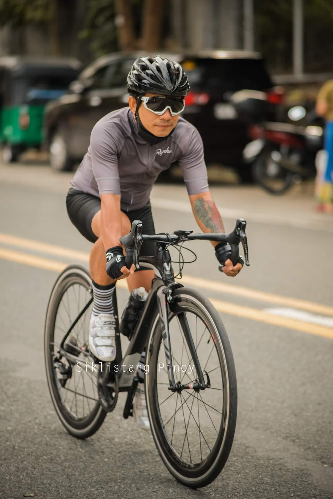Cyclist riding a SAVA carbon road bike on city street, wearing helmet and sports sunglasses