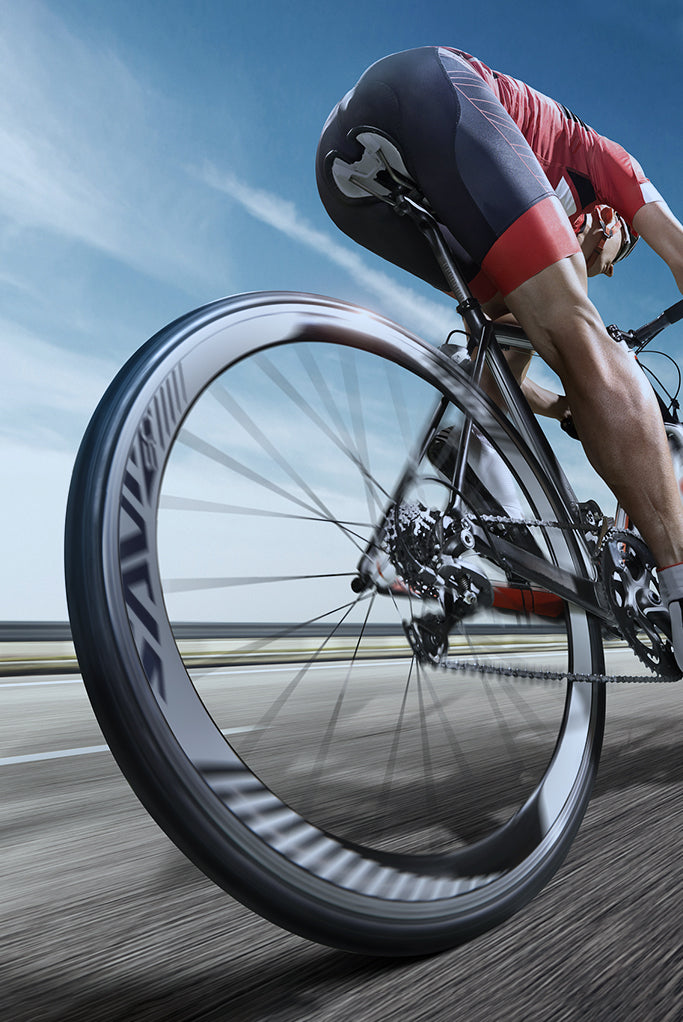 Cyclist riding SAVA carbon road bike at speed on open road, close-up of rear wheel