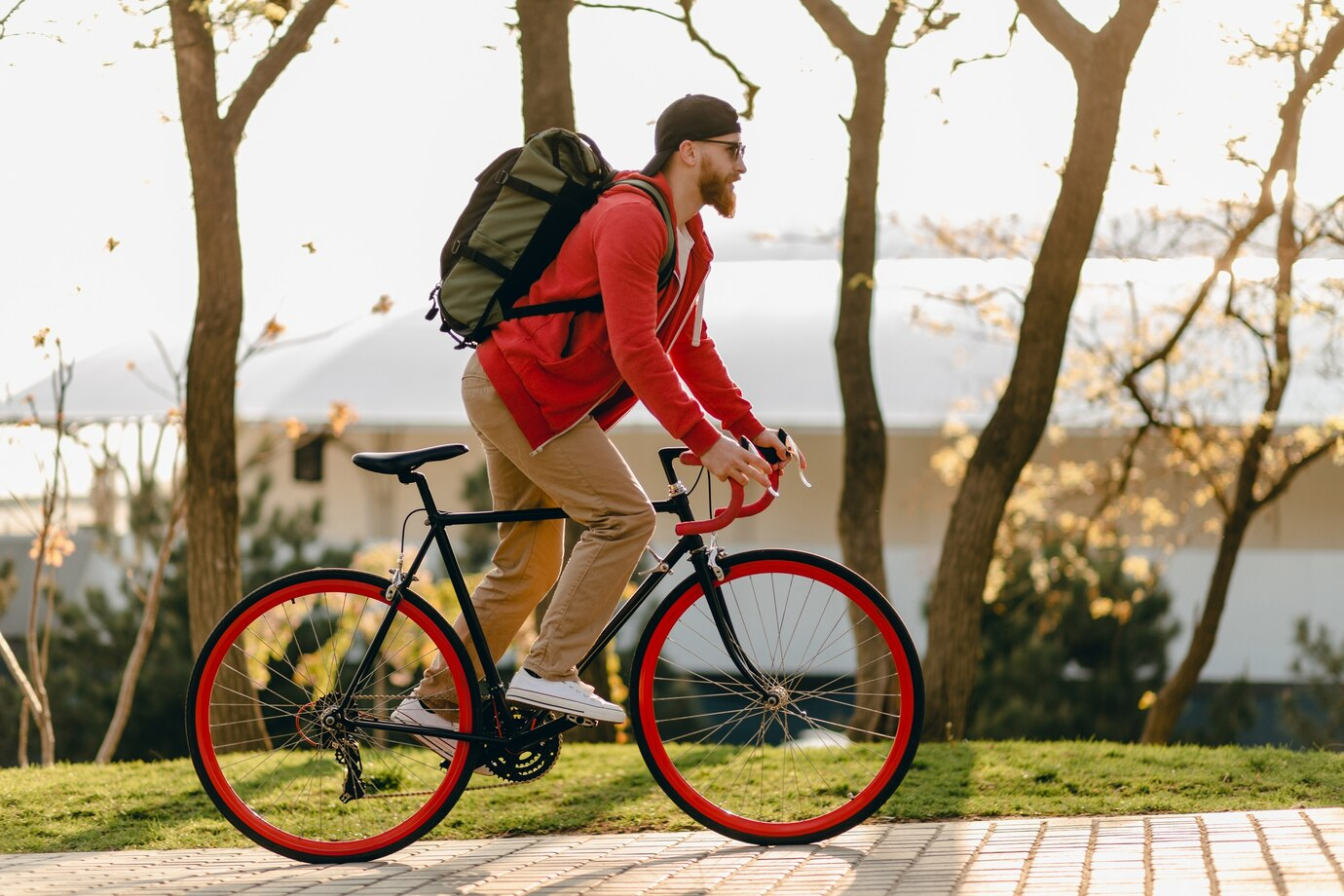 Man riding SAVA carbon bike with red rims outdoors, wearing backpack and cap