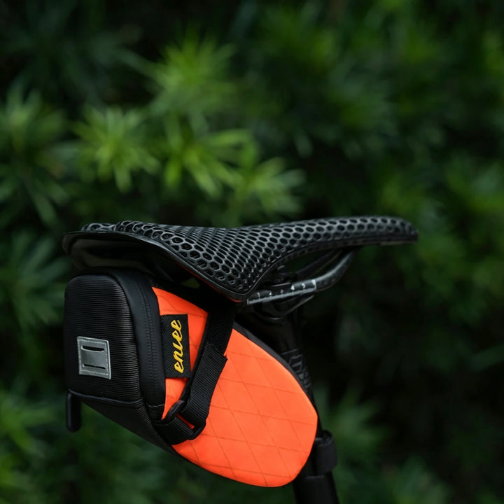 ENLEE 1.3L orange bicycle seat bag mounted under saddle with yellow logo detail outdoors.